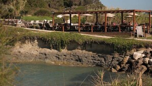 Ein Restaurant am Flussufer mit Außenbereich, einer Holzpergola und einer felsigen Uferlinie.