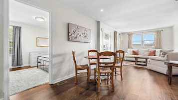 A spacious living room with a dining area, hardwood flooring, and a large window providing natural light.