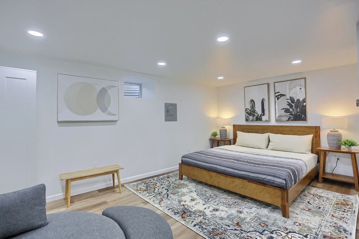 A bedroom with a bed, bedside tables, a bench, and artwork on the walls.