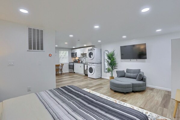 A modern living space with a kitchen, a grey sofa, a flat-screen TV, and a striped area rug.