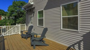 A deck with two Adirondack chairs and a small table, a white railing, and a house with grey siding and green window blinds. - Pittsburgh, Millvale Stylish 2BD with Parking (Millvale)