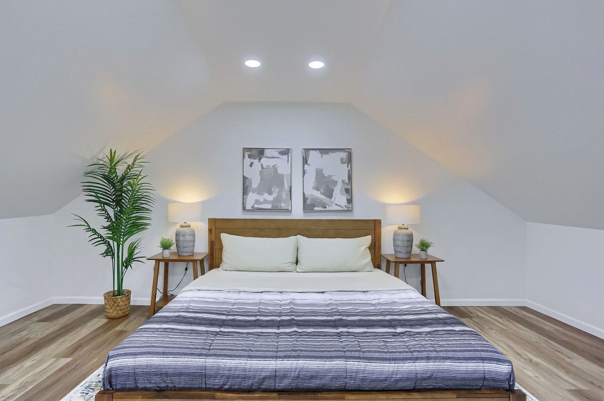 A bedroom with a bed, two bedside tables, a nightstand, a potted plant, and two wall-mounted picture frames.