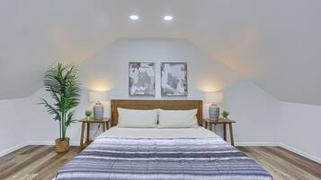 A bedroom with a bed, two bedside tables, a nightstand, a potted plant, and two wall-mounted picture frames.