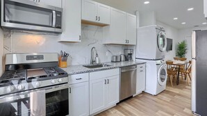 A modern kitchen with white cabinets, stainless steel appliances, a microwave, stove, sink, and a built-in washing machine. - Pittsburgh, Millvale Stylish 2BD with Parking (Millvale)