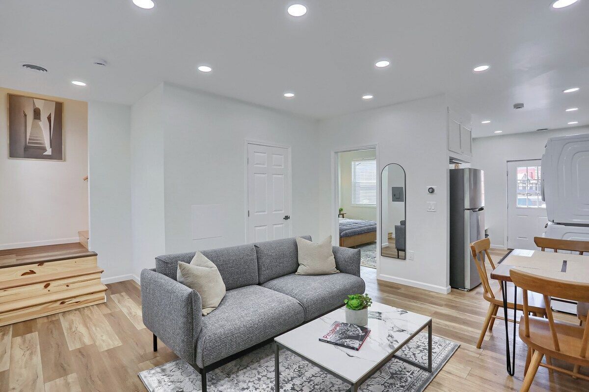 A modern living room with a grey sofa, a coffee table, and a dining area with wooden chairs.