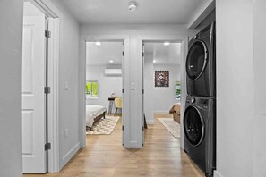 A modern interior with a laundry area, a bedroom with a bed and a desk, and a hallway leading to another room. - The Green House - Downtown Montrose (Montrose)