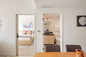 Een moderne hotelkamer met een bed, een zithoek met een tafel en stoelen, een kitchenette en een badkamer.