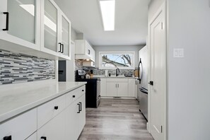 A modern kitchen with white cabinetry, a tiled backsplash, and a window with a view. - Comfortable East St. Paul Home | 3 Bed | 1 Bath | (East Saint Paul)