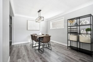 Zona pranzo con tavolo e sedie, un lampadario e una scaffalatura in metallo nero con cesti.