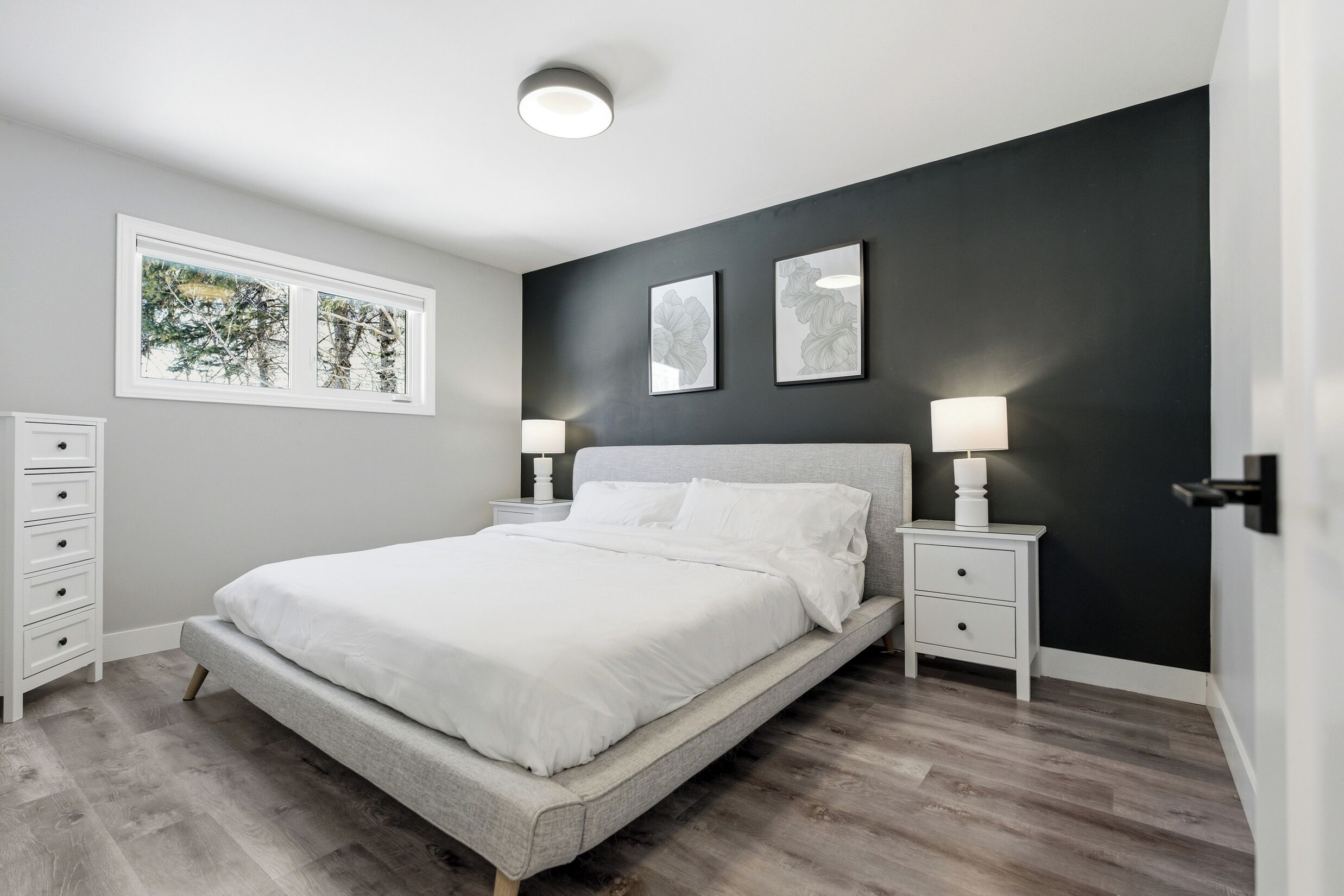 A bedroom with a bed, nightstands, a dresser, and artwork on the wall.