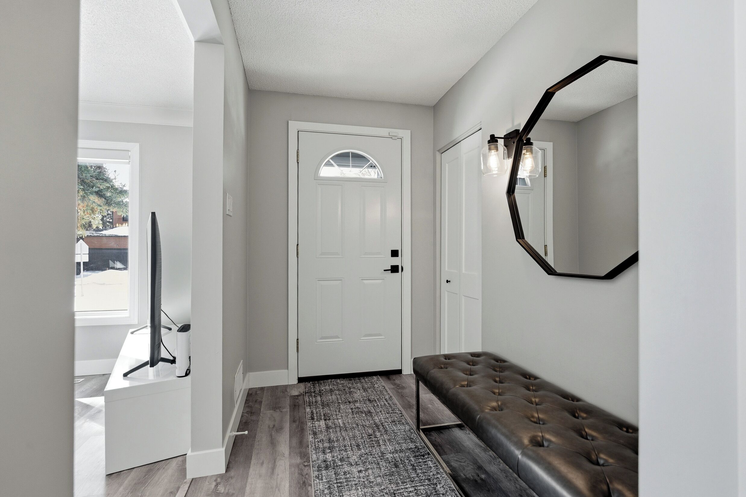 A hallway with a white door, a bench, a rug, and a wall-mounted light fixture.