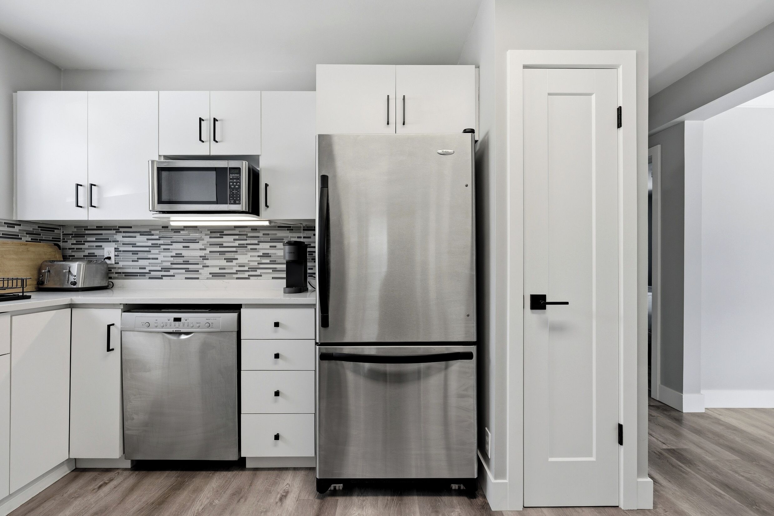 A modern kitchen with white cabinets, a stainless steel refrigerator, a microwave, and a dishwasher.