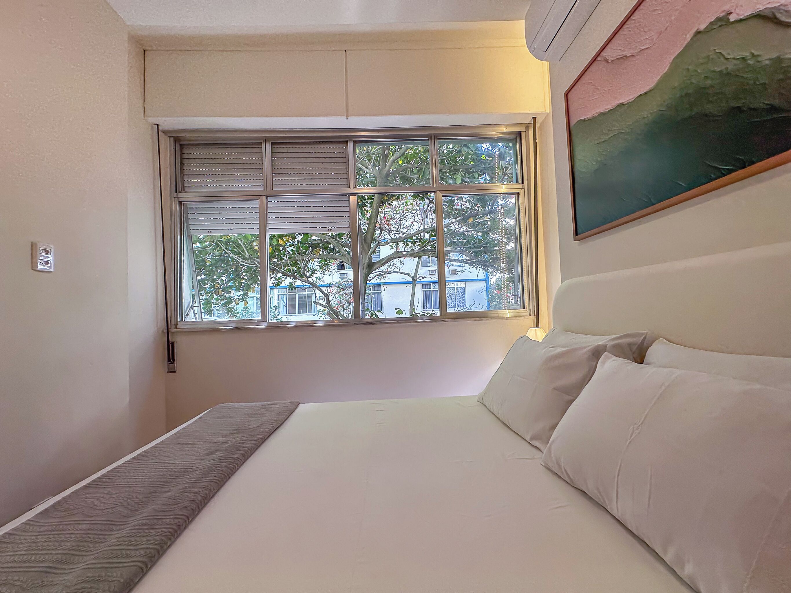 A bedroom with a bed, a window, and a painting on the wall.