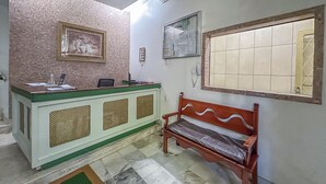 Un área de recepción con mostrador, una banca, un cuadro enmarcado, un tablón de anuncios y un ventanal con azulejos.
