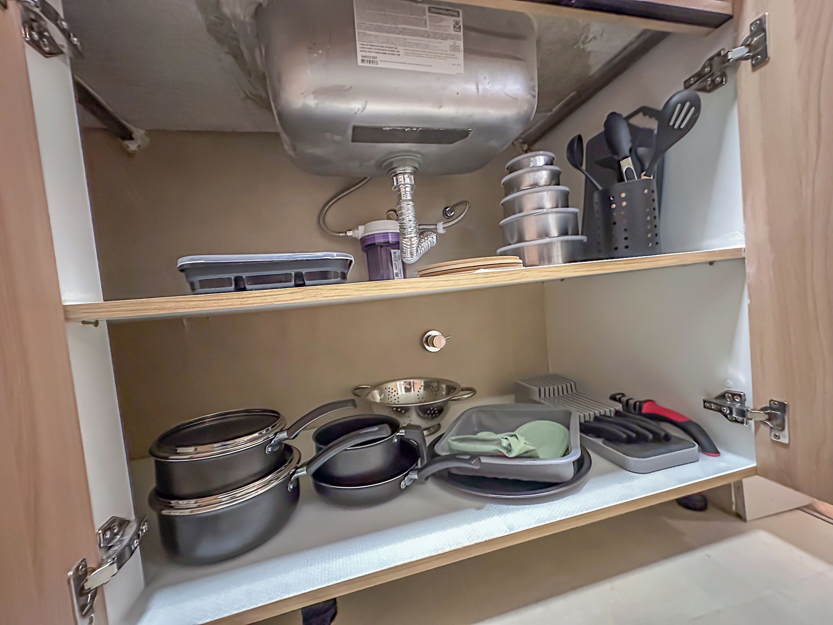Un meuble de cuisine contenant des ustensiles de cuisine, des couverts et un distributeur d’eau.