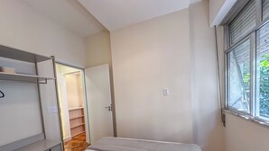 Quarto com cama, guarda-roupa, porta que dá para uma escada e janela com persianas.