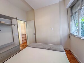 A bedroom with a bed, a wardrobe, a door leading to a staircase, and a window with blinds. - Copacabana: renovated, 3 min from the beach (Rio de Janeiro)