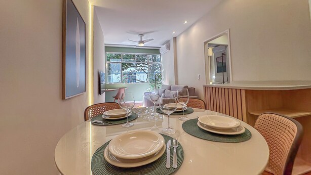 Uma sala de jantar com uma mesa redonda posta para quatro pessoas, com pratos, talheres e copos.