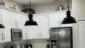 Una cocina moderna con gabinetes blancos, electrodomésticos de acero inoxidable e iluminación colgante negra.