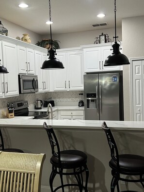 A modern kitchen with white cabinets, stainless steel appliances, and black pendant lighting.