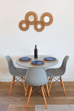 A round dining table with four grey chairs, a bottle of wine, and three glasses. - Luxury 2BR Escape - Steps to Beach & Restaurants (Oceanside)