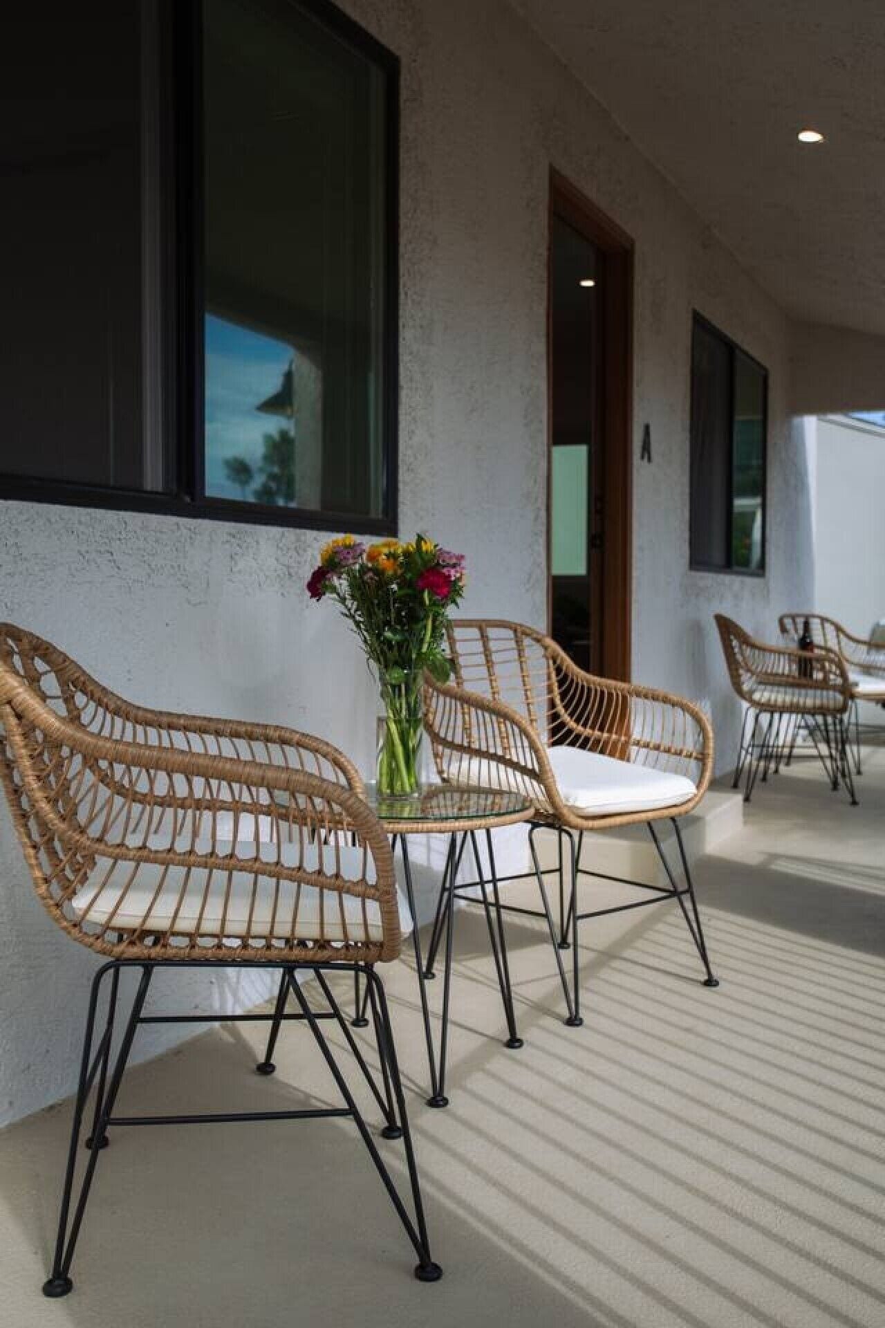 Fletstol med hynder, et glastbord og en vase med blomster på en balkon med udsigt til himlen.