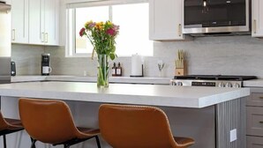 Una cocina moderna con armarios blancos, una isla central con taburetes, microondas empotrado e iluminación colgante.