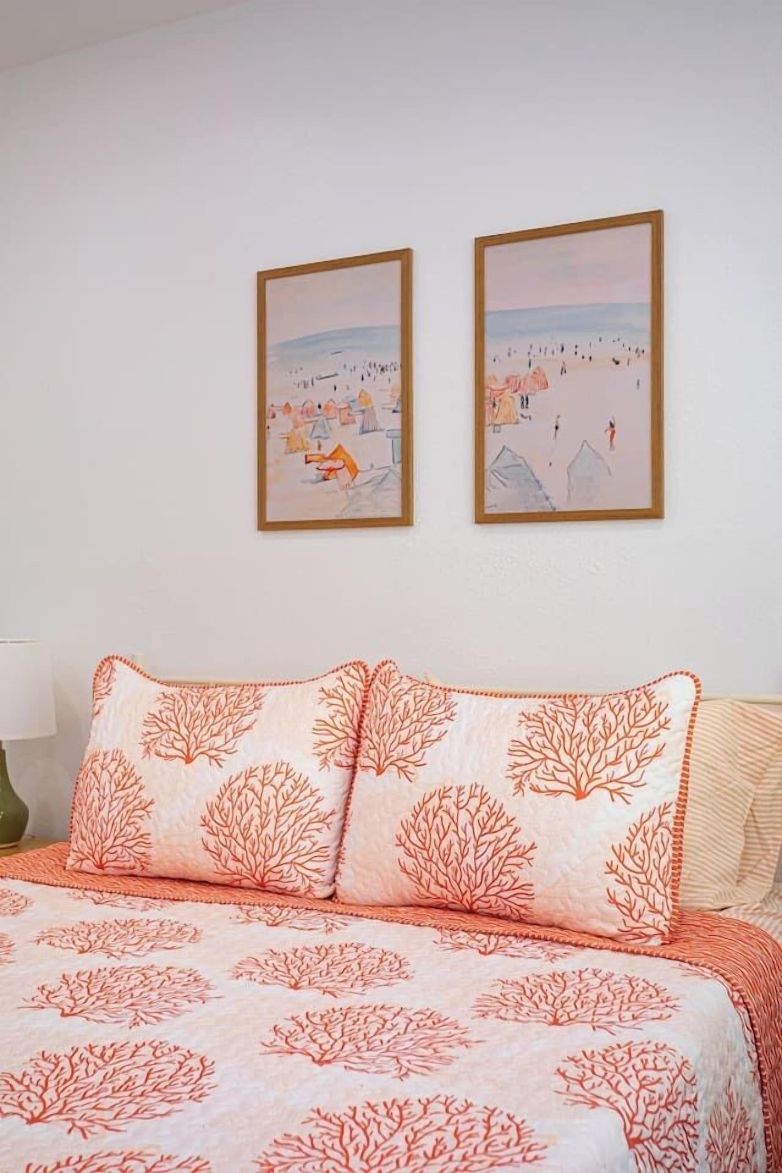 A bedroom with a bed, two framed artworks on the wall, and a patterned pillow.