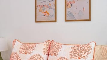 A bedroom with a bed, two framed artworks on the wall, and a patterned pillow.