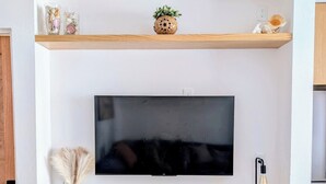 Ein Flachbildfernseher ist an einer Wand über einem Holzschrank montiert, auf dessen Ablage eine kleine Pflanze und Dekoration stehen.