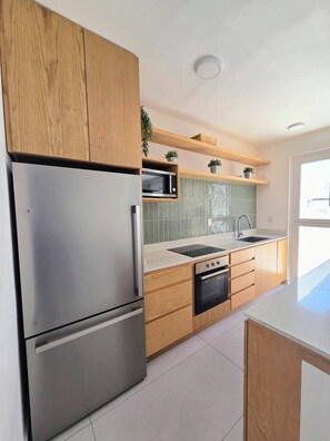 A modern kitchen with a stainless steel refrigerator, wooden cabinets, a microwave, and a dishwasher. - Modern Coastal Oasis with Private Pool (Puerto Morelos)
