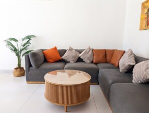 A modern living room with a grey sectional sofa, a round wooden coffee table, and a potted plant. - Modern Coastal Oasis with Private Pool (Puerto Morelos)