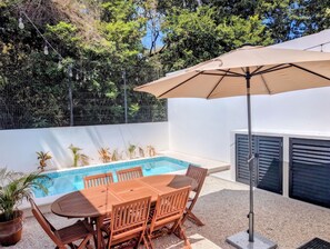 A poolside area with a table and chairs, a hanging light fixture, and a large umbrella. - Modern Coastal Oasis with Private Pool (Puerto Morelos)