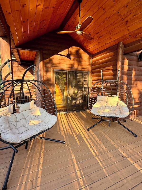 A log cabin with two hanging chairs and a ceiling fan.