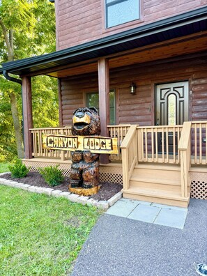 A wooden cabin with a bear sculpture on the porch, a wooden deck, and a sign reading 'CANYON LODGE'.