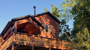 Eine zweistöckige Blockhütte mit Balkon, Schornstein und rustikalem Natursteinfundament.