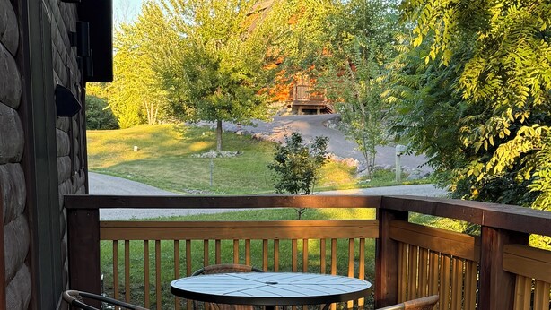 Eine Holzterrasse mit einem runden Tisch und vier Korbstühlen.