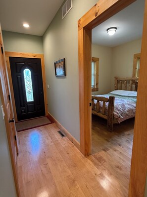 A hallway leading to a bedroom with a wooden bed frame and a door with a stained glass window.