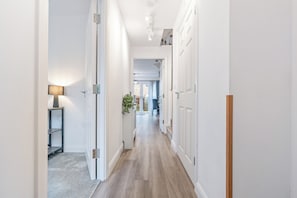 A hallway with white walls, a wooden floor, and a lamp on a shelf. - Modern 4BR City Centre Home | Sleeps 8 | FREE Parking | Garden (Birmingham)