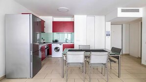 A modern kitchen with a refrigerator, oven, and washing machine, a dining area with a table and chairs, and a hallway with a door. - THE PERFECT COMBINATION OF COMFORT, CONVENIENCE & A PRIME CENTRAL LOCATION. (Cannes)
