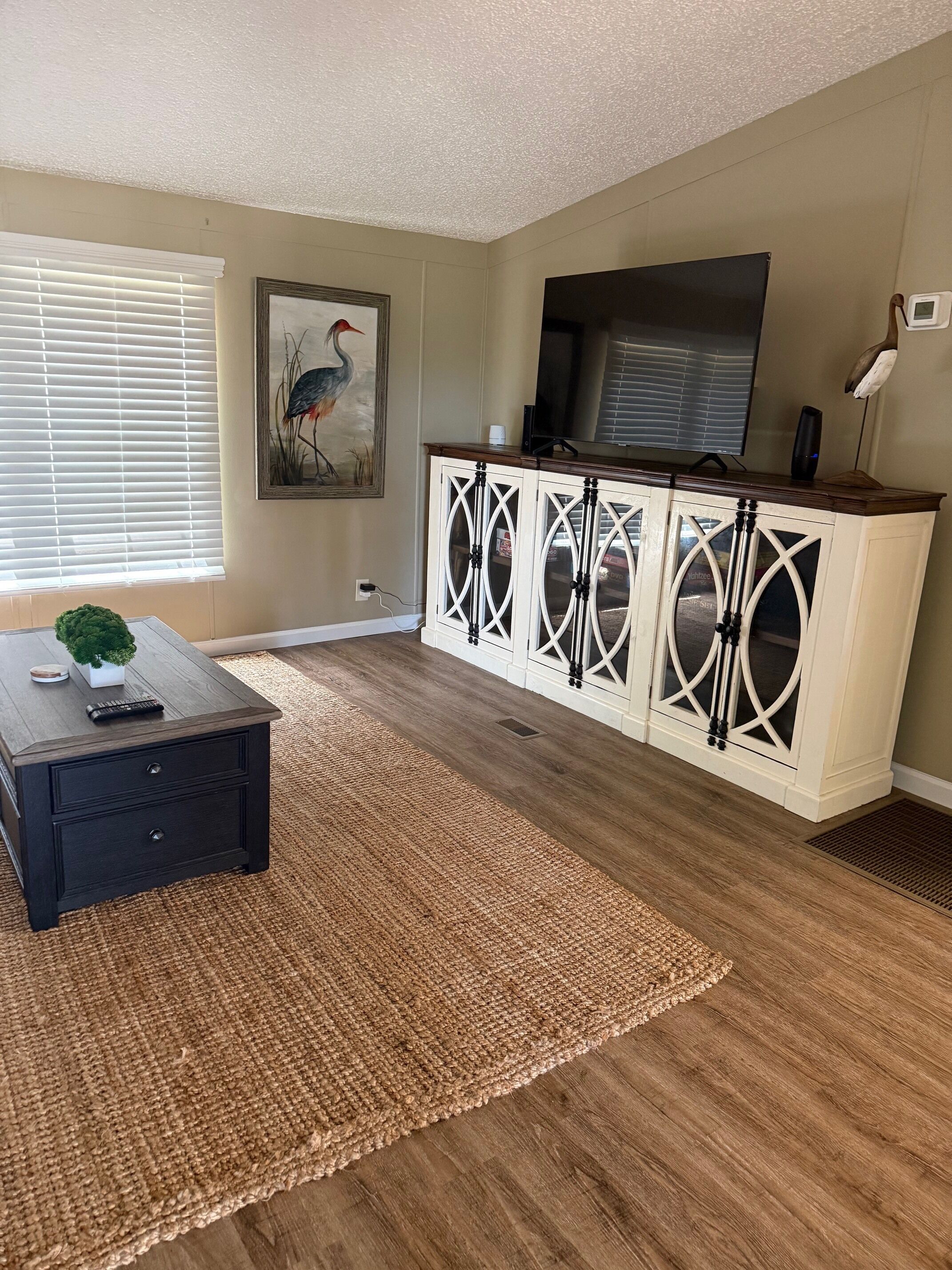 A living room with a dark wood coffee table, a woven rug, a white cabinet with glass doors, and a flat-screen TV on a stand.