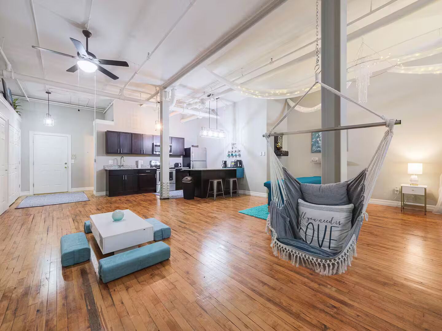 A spacious living area with a hanging chair, a kitchen in the background, and a wooden floor.
