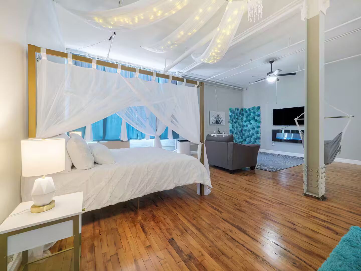 Ein Schlafzimmer mit Himmelbett, grauem Sofa, Fernseher und einer Hängematte.