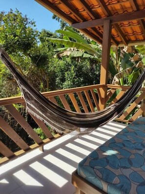 A hammock on a wooden deck with a view of greenery.