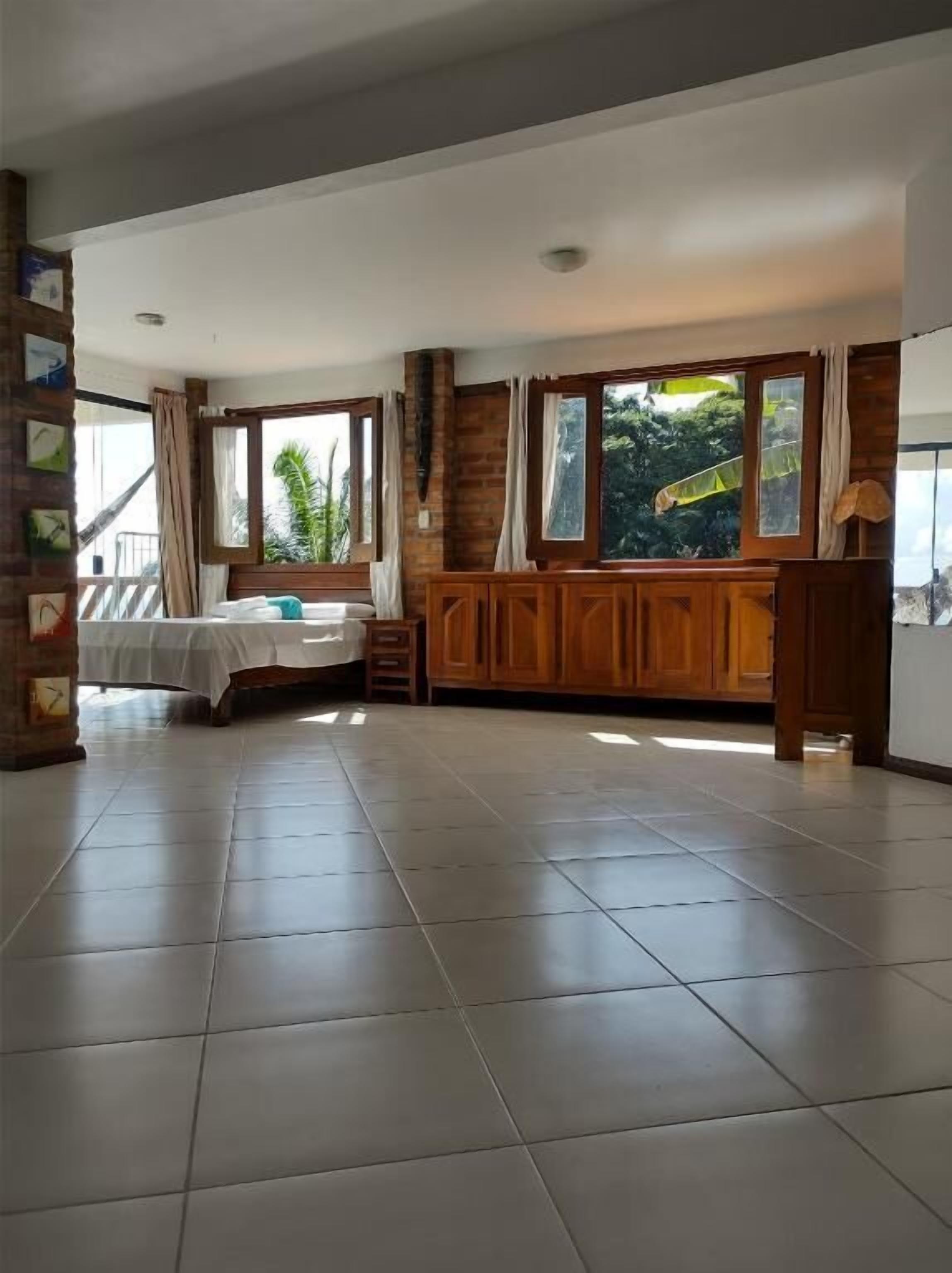 Quarto espaçoso com cama, um armário de madeira e janelas amplas com vista para o verde.