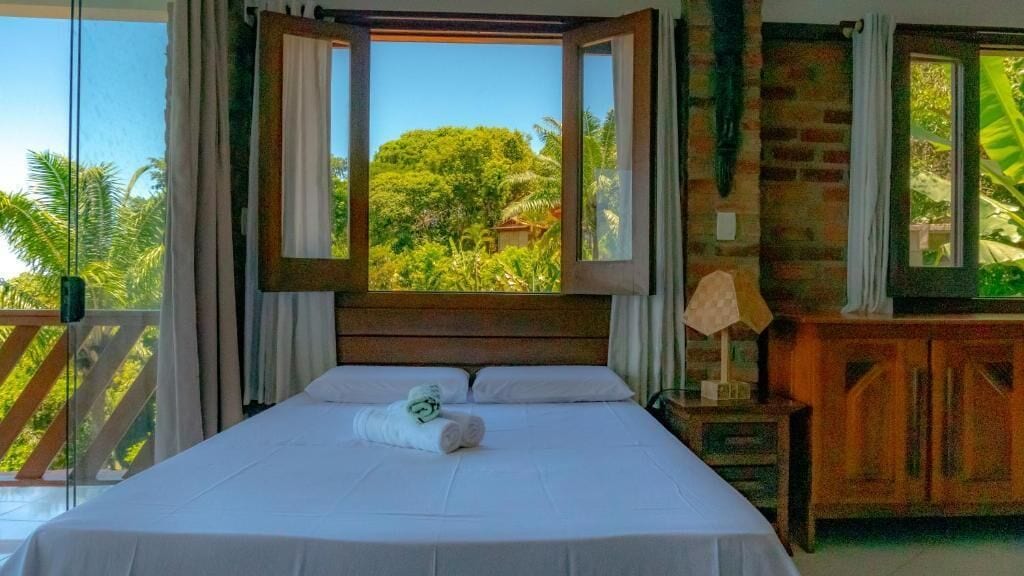 Una cama con vistas al verdor, un cabecero de madera y una mesita de noche con una lámpara.