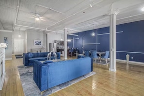 A modern interior with a blue sofa set, a dining area, and a kitchen in the background. - Blue Dream Downtown/POOL TABLE (Detroit)