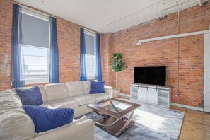 Ein Wohnzimmer mit Backsteinwand, einer Sofagarnitur, einem Fernseher und einer Pflanze.