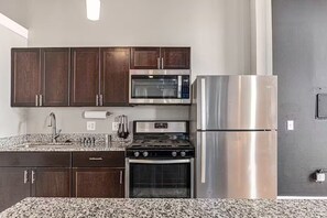 A kitchen with dark wooden cabinets, a stainless steel refrigerator, a microwave, a stove, and a sink. - Casual corner (Detroit)