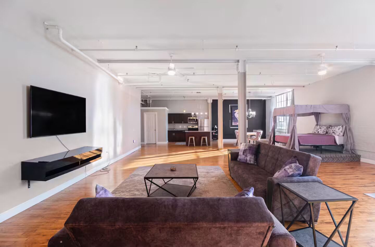 A modern living room with a flat-screen TV, a sofa, a coffee table, and a dining area in the background.